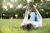 Junge Frau mit Smartphone im Park liegend, Orgeval