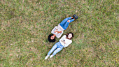 Junge Freundinnen liegen im Gras und benutzen ihr Smartphone im Park, Orgeval