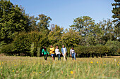 Fröhliche junge Freunde spazieren durch eine Wiese im öffentlichen Park