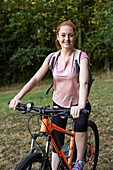 Lächelnde junge Frau auf Fahrrad im Wald sitzend