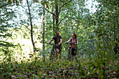 Smiling young couple walking with bicycles in forest