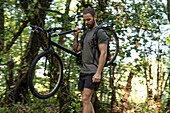 Junger Mann mit Fahrrad im Wald