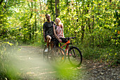 Smiling young couple standing with bicycles in forest