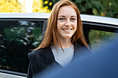 Lächelnde junge Frau steht vor einem Auto