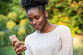 Nahaufnahme einer lächelnden jungen Frau, die im Park ein Smartphone benutzt