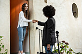 Smiling young female friends shaking hands at doorstep