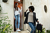 Young female friends waving hands at doorstep