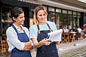 Mid-shot von zwei Unternehmerinnen, die vor ihrem Restaurant eine Liste prüfen