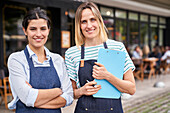 Mittlere Einstellung von zwei Restaurantbesitzerinnen, die in die Kamera schauen, während sie vor ihrem Restaurant stehen