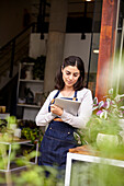 Garden center female worker taking inventory on digital tablet