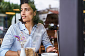 Porträtaufnahme einer lateinamerikanischen Frau, die in einem Café sitzt, durch ein Fenster
