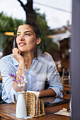 Blick durch das Fenster auf eine in Gedanken versunkene lateinamerikanische Frau im Café