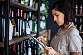 Wine store female worker taking inventory on digital tablet