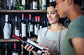 Mitarbeiter einer Weinhandlung lesen das Etikett einer Weinflasche, während sie in einem Raum stehen