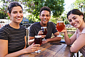 Medium-shot of three friends looking at camera while having a good time drinking beer at a trendy outdoors bar
