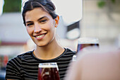 Junge Frau lächelt und schaut in die Kamera, während sie an einer Bar im Freien sitzt