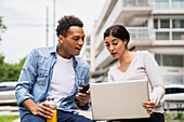 Mid-shot of African-American man and Latin American woman using laptop while working outdoors