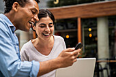 Side shot African-American man and Latin-American woman looking at a smartphone screen and laughing