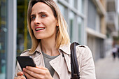Mid-shot of attractive woman looking for somebody while holding a cell phone in her hand