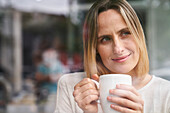 Porträt einer attraktiven Frau mit einer Tasse Kaffee in der Hand, die den Moment genießt