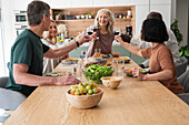 Eine Gruppe verschiedener älterer Freunde stößt beim Abendessen zu Hause an