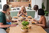 Gruppe von verschiedenen Freunden mittleren Alters, die sich beim Mittagessen zu Hause über ihre Erlebnisse austauschen
