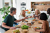 Eine Gruppe älterer Freunde stößt an, während sie zu Hause gemeinsam essen