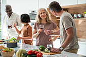 Eine Gruppe verschiedener Freunde mittleren Alters unterhält sich in der Küche, während sie Essen zubereiten
