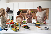Eine Gruppe älterer Freunde versammelt sich um die Kücheninsel, während sie das Essen zubereiten