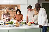Group of diverse middle-aged friends chatting at kitchen island while cooking meal