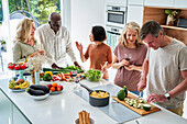 Group of seniors friends gathered at kitchen while preparing dinner