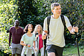 Mann mittleren Alters mit Rucksack und Wanderstöcken beim Wandern im Wald mit einer Gruppe von Freunden