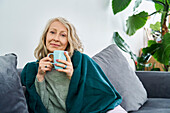 Ältere Frau sitzt auf der Couch und hält eine Tasse Tee