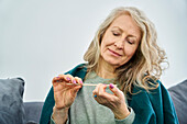 Senior woman sitting on sofa while filing nails