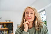 Thoughtful senior woman with hand on chin sitting in dining room