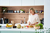 Attratktive Frau mittleren Alters schneidet Obst in ihrer Küche