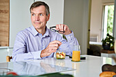 Berufstätiger Mann mittleren Alters frühstückt zu Hause an der Küchentheke