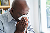 Nahaufnahme eines älteren afroamerikanischen Mannes mit Erkältung, der sich die Nase schnäuzt