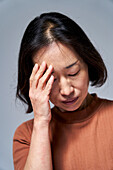 Reife asiatische Frau mit Kopfschmerzen