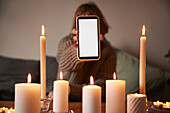 Frau zeigt Telefon über brennende Kerzen