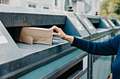 Frauenhand, die eine Pappschachtel in die Recycling-Tonne steckt