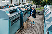 Frau wirft Karton in die Recycling-Tonne