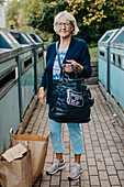 Woman with paper bags at recycling bins
