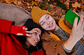 Freunde machen ein Selfie auf dem Boden liegend in einer Herbstlandschaft