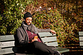 Mann sitzt auf einer Bank und telefoniert im Herbstpark