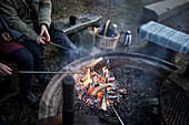 People preparing hotdogs over campfire