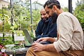 Smiling men using laptop in greenhouse