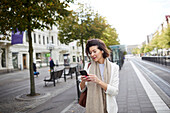 Lächelnde Geschäftsfrau, die ein Smartphone auf der Straße benutzt