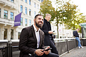 Smiling businessmen using phones in city