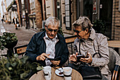 Senior couple using phones in sidewalk cafe